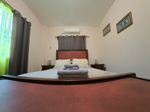 A neatly made bed with pillows and a folded towel, a bedside table with a lamp, and a wall-mounted air conditioner. - Julie Grove Peaceful 2-bedroom apartment with AC in charming Kelly Village (Kelly Village)
