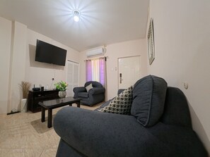 A living room with a sofa, a television, a coffee table, and a decorative vase. - Julie Grove Peaceful 2-bedroom apartment with AC in charming Kelly Village (Kelly Village)