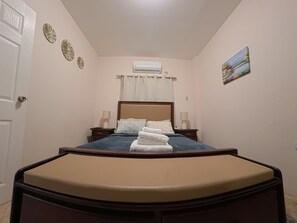 Une chambre à coucher comprenant un lit, des tables de chevet, un appareil de climatisation, une porte et un élément de décoration murale.