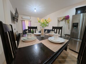 A dining area with a dark wooden table set for two, a vase with flowers, and a modern refrigerator. - Julie Grove Peaceful 2-bedroom apartment with AC in charming Kelly Village (Kelly Village)