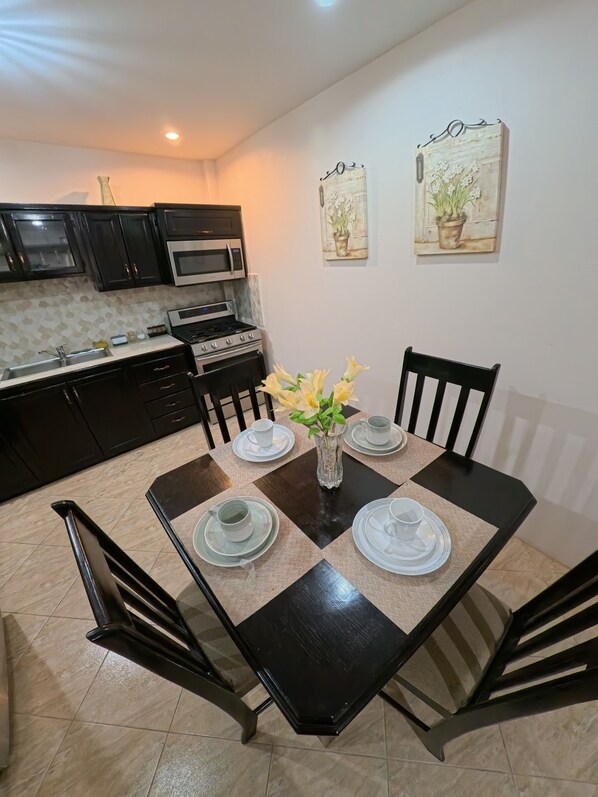 Un coin repas avec une table noire dressée pour quatre personnes, entourée de chaises, et un vase avec des fleurs posé sur la table.