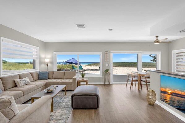 Un salon spacieux doté d’une grande fenêtre donnant sur une plage, d’un coin salon confortable et d’une cuisine avec vue.