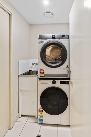 Ein kleiner Waschraum mit einer Waschmaschine und einem Trockner mit Frontlader, einem Handwaschbecken und einem Schrank.