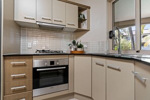 Une cuisine moderne équipée d’un four Bosch, d’une cuisinière à gaz et d’une fenêtre donnant sur des palmiers.