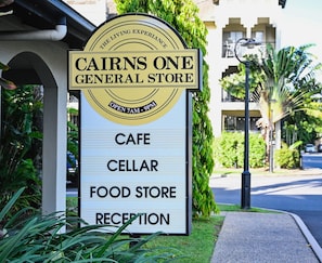 A sign for Cairns One General Store listing its amenities: cafe, cellar, food store, and reception. - Stunning Resort Apartment With Gym and Pool Access (Cairns)