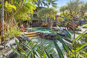 A tropical resort with a pool surrounded by rocks and lush greenery. - Stunning Resort Apartment With Gym and Pool Access (Cairns)