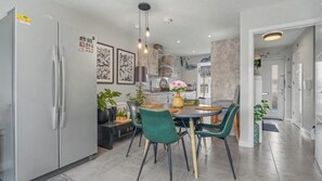 A modern kitchen with a dining area, featuring a refrigerator, a stove, and a dining table with chairs. - Fully Furnished 3 Bed House-Blythe Valley Park Shirley B90 8AY (Shirley Solihull)