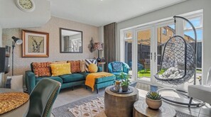 A modern living room with a sofa, armchairs, a hanging chair, and a large window. - Fully Furnished 3 Bed House-Blythe Valley Park Shirley B90 8AY (Shirley Solihull)