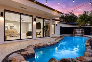 A swimming pool with a stone border and a waterfall feature, surrounded by a patio area with outdoor furniture. - Mega-Yacht Showcase Villa with Pool Table/Marble (Fort Lauderdale)