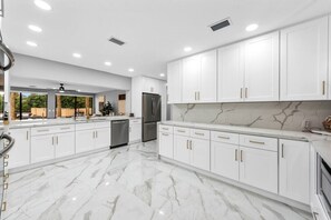 Une cuisine moderne avec des meubles blancs, un revêtement de sol en marbre et des appareils électroménagers en acier inoxydable.