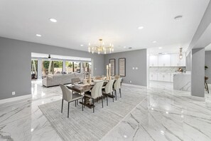 A spacious dining area with a marble floor, a chandelier, and a view of a backyard. - Mega-Yacht Showcase Villa with Pool Table/Marble (Fort Lauderdale)