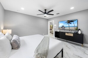 Ein Schlafzimmer mit Bett, Deckenventilator, Fernseher und Blick auf den Strand.