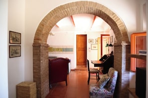 An arched doorway leading to a room with a wooden door, a chair, a small table, and a lamp. - The Pietraio Guardistallo (Guardistallo)