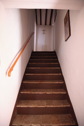 A staircase with wooden steps and a handrail, leading to a landing with a light switch and a small wall-mounted light fixture. - The Pietraio Guardistallo (Guardistallo)