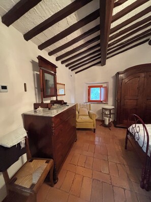 A traditional room with a wooden dresser, a chair, a bed, and a window with a view. - The Pietraio Guardistallo (Guardistallo)