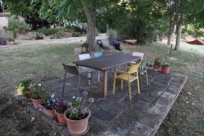 An outdoor patio area with a wooden table and chairs, surrounded by potted plants and a grassy lawn. - The Pietraio Guardistallo (Guardistallo)