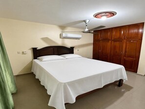 Ein Einzelbett mit Holz-Kopfteil, einem Deckenventilator und einem Schrank mit mehreren Türen.