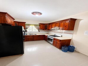 Eine Küche mit Holzschränken, einem schwarzen Kühlschrank, einem Herd und einem Spülbecken.