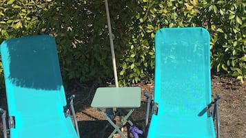 Two turquoise lounge chairs with a thatched umbrella and a small table in a garden setting.