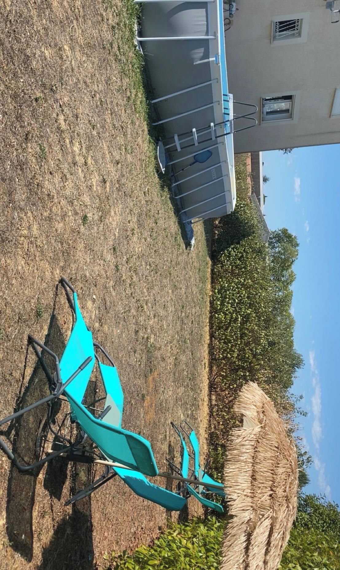 Ein blauer Rasensessel und ein Heuballen in einer grünen Wiese, im Hintergrund ein Gebäude.