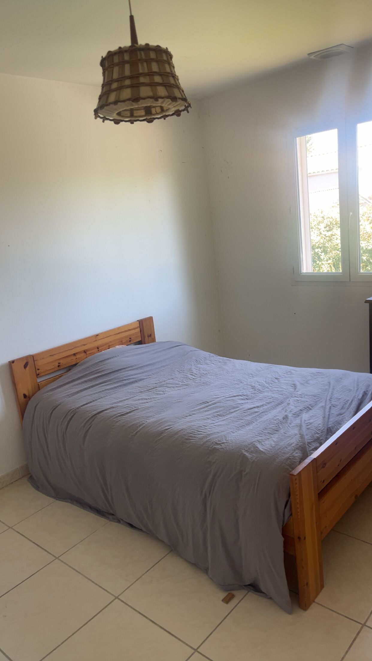 A room with a single bed, a window, and a hanging light fixture.