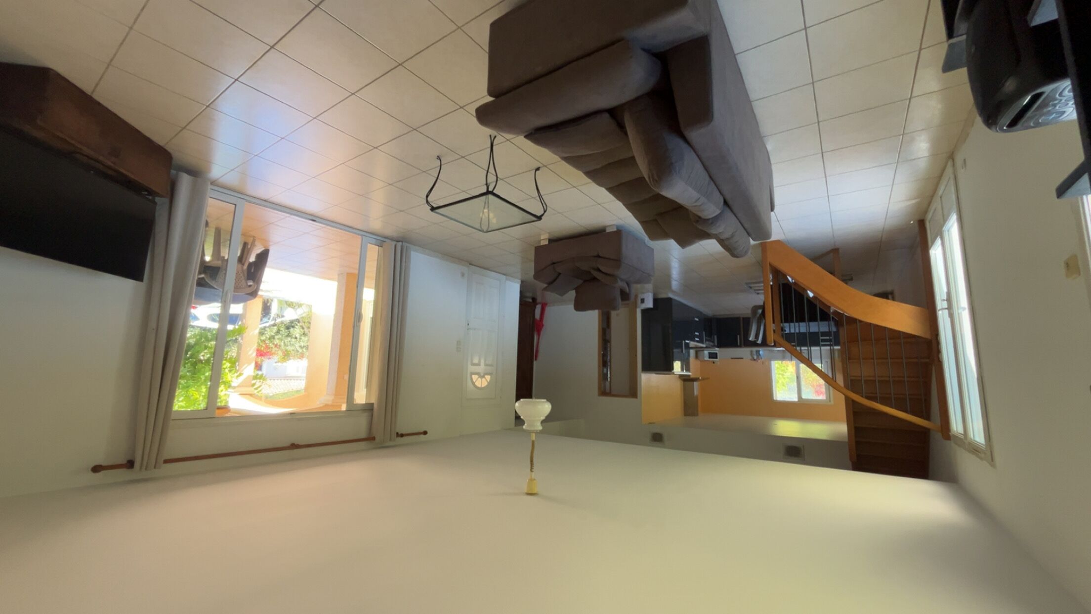 Een ruime kamer met een groot raam, een trap en een plafond met een bijzonder ontwerp.