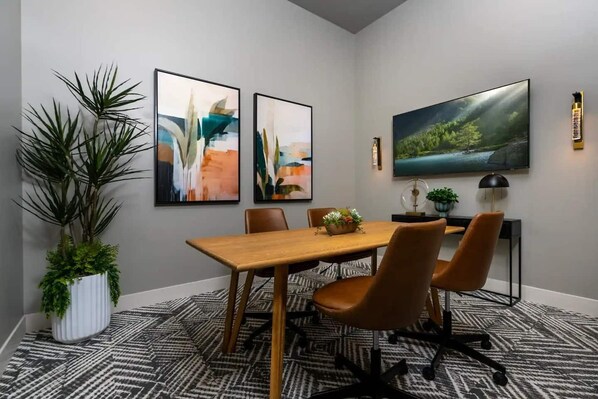 A modern dining area with a wooden table, four chairs, abstract paintings, a large TV, and a potted plant.