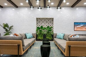A modern lounge area with two sofas, a central plant, and a patterned wall.