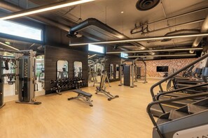 A gym with various exercise equipment, wooden flooring, and large windows allowing natural light.