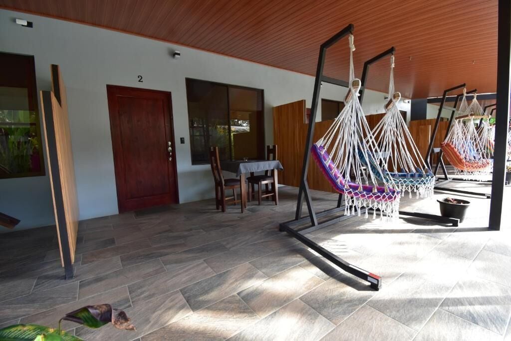 Quarto com teto de madeira, área de jantar com mesa e cadeiras, e espaço com várias redes.