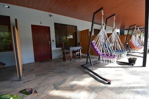 A room with a wooden ceiling, a dining area with a table and chairs, and a hammock area with multiple hammocks.