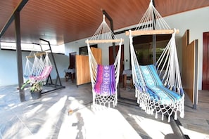 A room with three hammocks, wooden flooring, and a large window allowing natural light. - Raya (Matapalo)