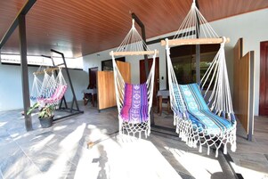 A room with three hammocks, wooden flooring, and a large window allowing natural light.