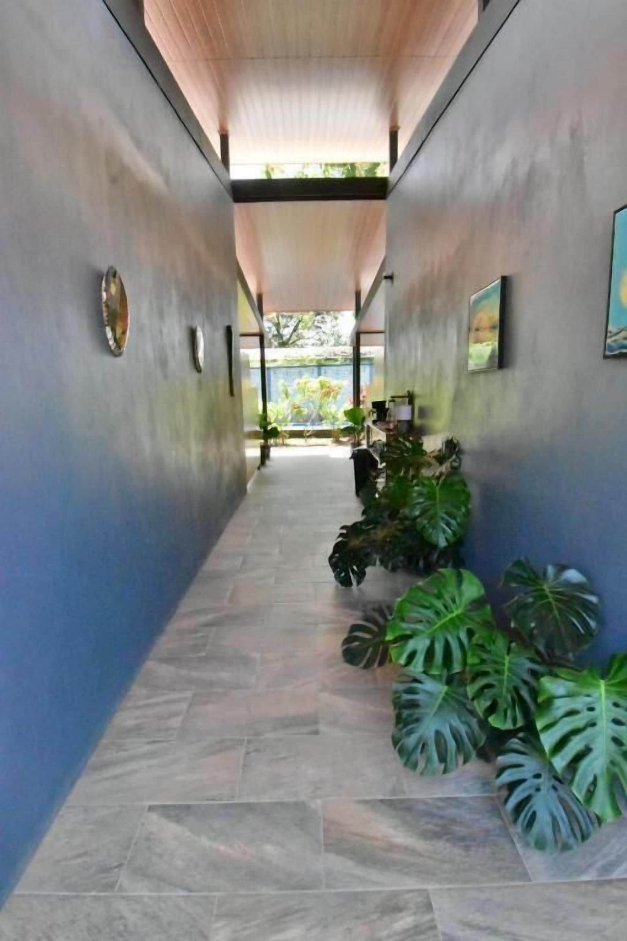 A corridor with a tiled floor, potted plants, and framed artwork on the walls.