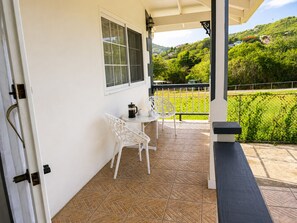 Eine überdachte Terrasse mit Tisch und Stühlen, ein Fenster und Blick auf eine grüne Landschaft.