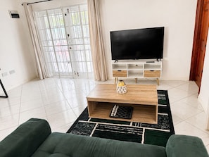 A modern living room with a flat-screen TV, wooden coffee table, and green sofas. - Maison Teranga- 70m2, 2-BRM apartment, with AC, 5 minutes drive to Rodney Bay (Gros Islet)