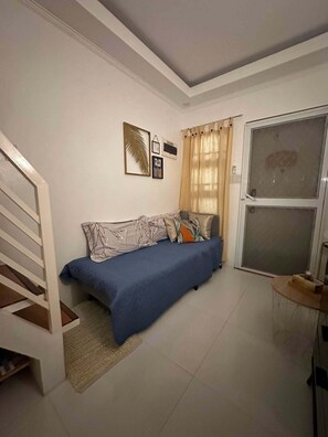Un dormitorio con cama, una ventana con cortinas, una puerta y una escalera.