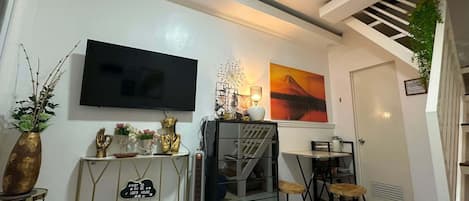 A modern living room with a flat-screen TV, a staircase, and a dining area.