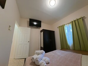 Ein Schlafzimmer mit einem Bett, einem an der Wand montierten Fernseher, einem Kleiderschrank und einem Fenster mit Vorhängen.
