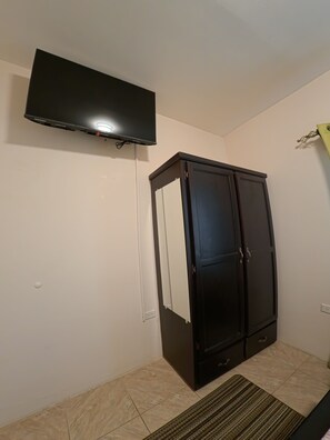 Ein Zimmer mit einem Wand-Fernseher, einem dunklen Holzschrank und einem gemusterten Teppich.