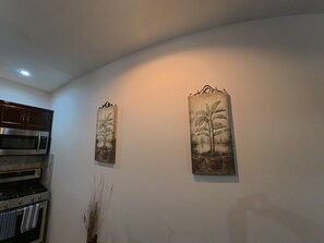 Eine Küche mit Mikrowelle, Backofen und Schränken. Zwei an der Wand befestigte Pflanzenbilder.