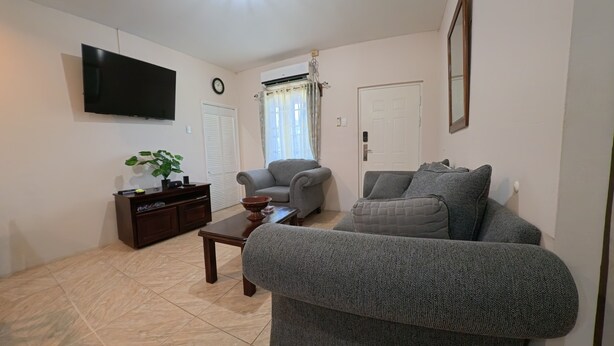 Ein Wohnzimmer mit Sofa, Couchtisch, Fernseher, einer Uhr und einer Tür.
