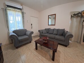 A living room with two grey sofas, a wooden coffee table, and a door with a mirror above it. - Sweet Escape Welcoming  2-bedroom apartment  Kelly Village with AC comfort (Kelly Village)