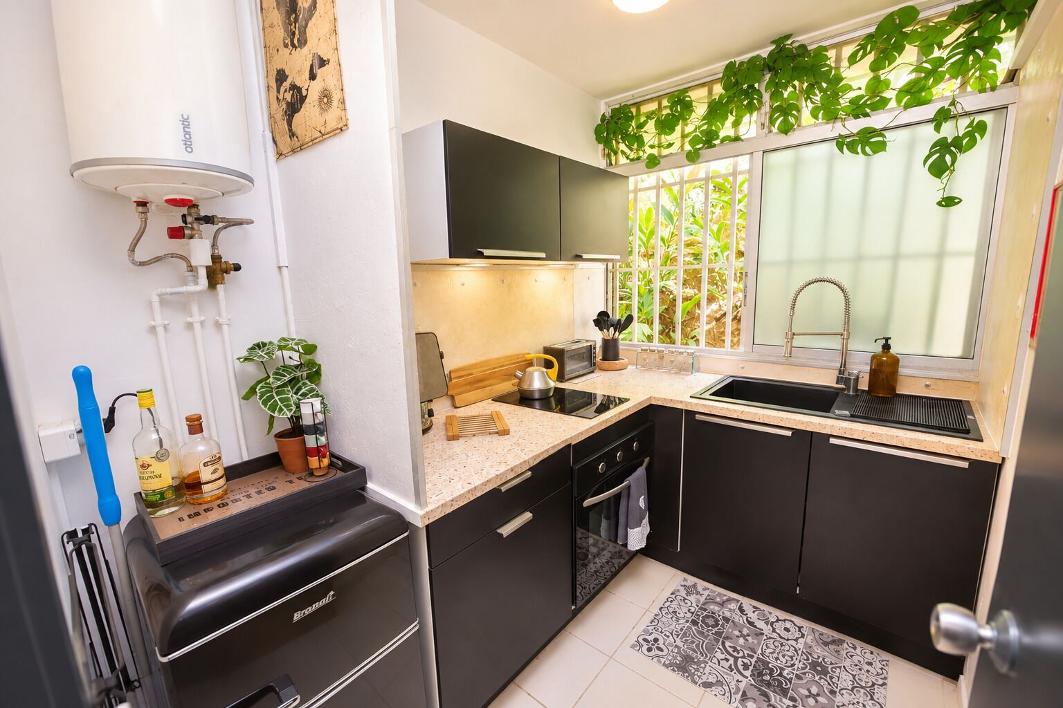 A compact kitchen with a built-in dishwasher, a sink, and a stove. There is a window with a view of greenery outside.