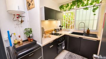 A compact kitchen with a built-in dishwasher, a sink, and a stove. There is a window with a view of greenery outside.