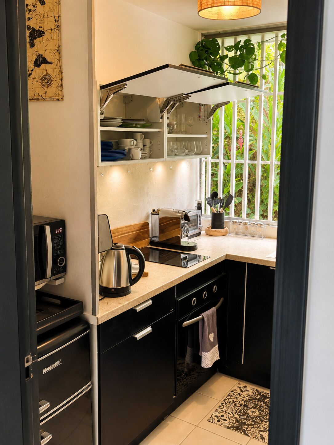 A modern kitchen with black cabinets, a stainless steel refrigerator, a coffee maker, and a window with a view of greenery.