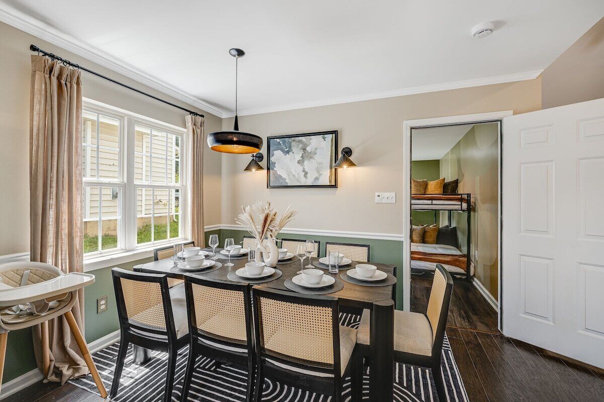 A dining area with a table set for four, surrounded by chairs, a baby high chair, and a window with curtains.