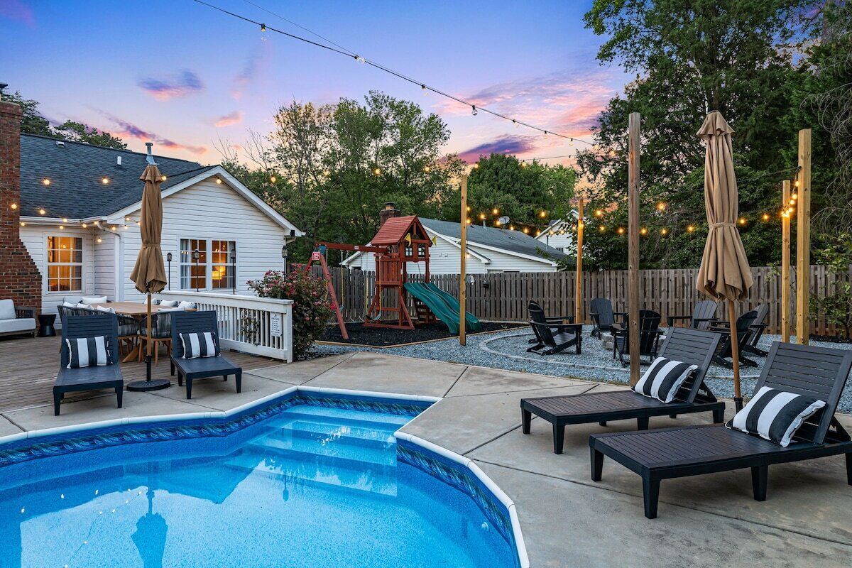 A backyard with a swimming pool, lounge chairs, a wooden play structure, and string lights.