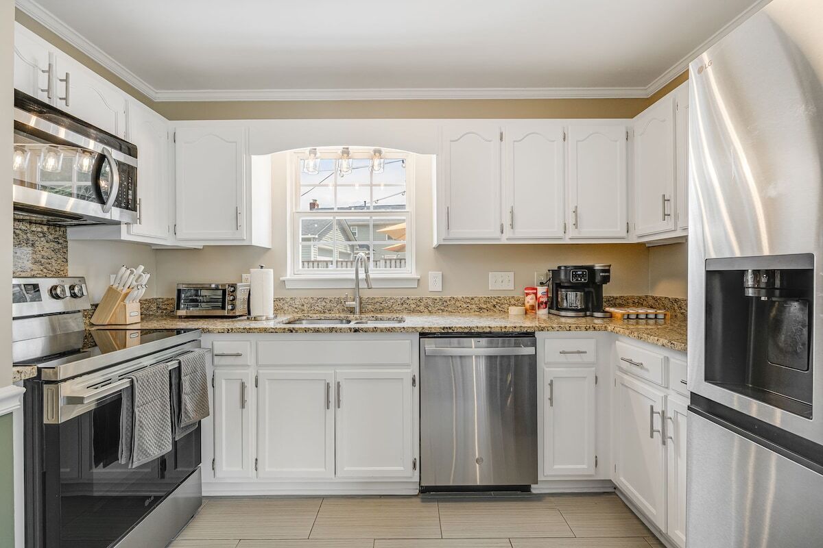 A modern kitchen with white cabinets, stainless steel appliances, and a window providing natural light.