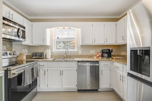 A modern kitchen with white cabinets, stainless steel appliances, and a window providing natural light. - 4BR Backyard Oasis: Pool, Hot Tub & Fire Pit (Charlotte)